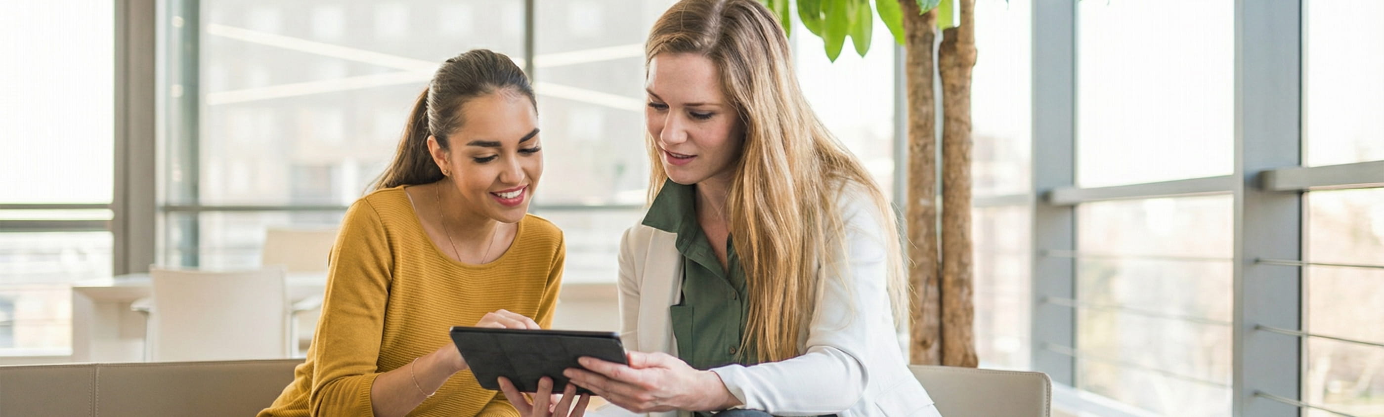 Duas mulheres sentadas num ambiente interior moderno a analisar um tablet juntas, cenário associado à consulta de informação e avaliação do valor patrimonial tributário e impacto no crédito habitação.