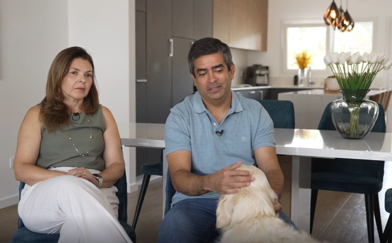 Casal sentado lado a lado em ambiente doméstico com cozinha ao fundo, cenário associado ao testemunho de Ricardo e Elizete Calumby e a sua experiência com a UCI.
