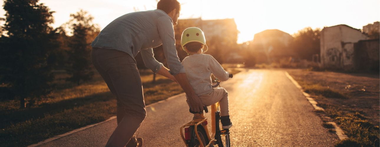 Pai a ensinar o filho a andar de bicicleta. Cenário representado pelo pôr do sol. Cenário associado à família e a uma solução de crédito habitação que acompanhe os diferentes momentos da vida.