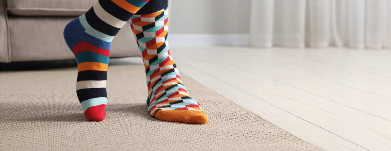 Pés com meias coloridas sobre um tapete numa habitação luminosa, cenário associado ao conforto do lar.