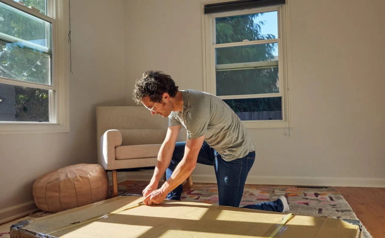 Homem num quarto a montar mobiliário em casa junto a uma janela com luz natural, cenário associado ao crédito para comprar casa e obras.