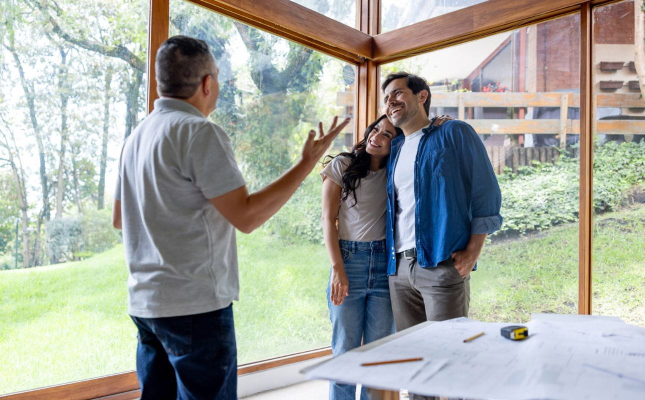 Arquiteto a falar com casal a duas pessoas numa habitação com amplas janelas e vista para o exterior, cenário associado ao crédito para construção