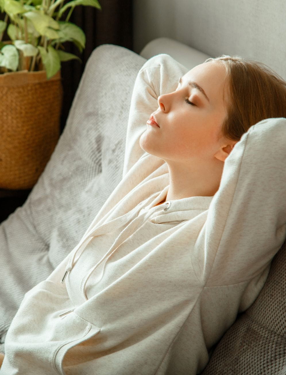 Mulher sentada confortavelmente num sofá junto a uma janela com luz natural e plantas de interior, cenário associado à transferência de crédito habitação.