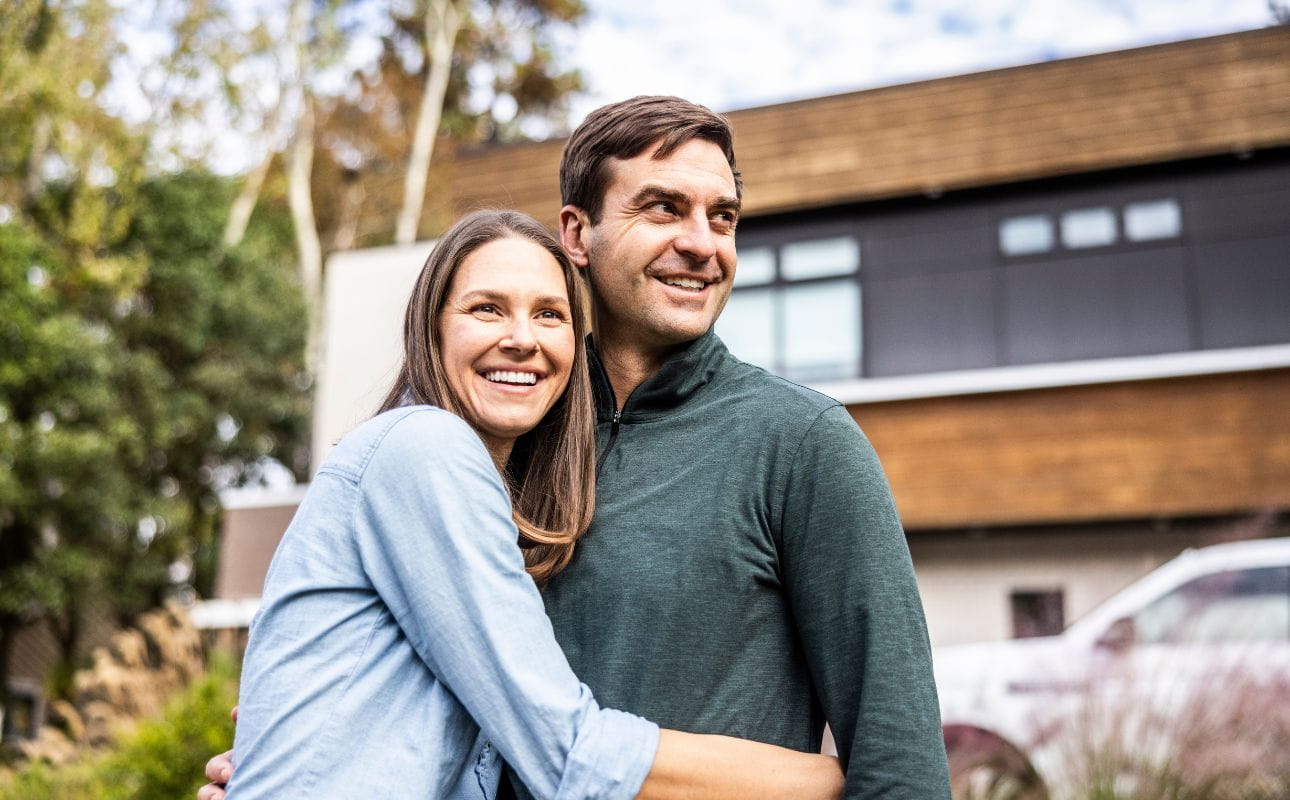 Um casal em frente a uma moradia moderna rodeada de natureza, cenário associado à transferência de crédito habitação.